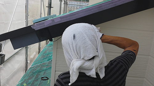 730_hafu-uwanuri2 | 外壁塗装は神奈川県横浜市の塗装職人 Construction worker with a towel wrapped over their head, standing beside a house under construction and working on the eave near scaffolding.