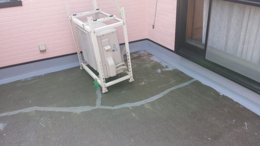METADATA-START | 外壁塗装は神奈川県横浜市の塗装職人 Outdoor HVAC condenser unit on a white metal frame on a pink-walled rooftop balcony beside a sliding glass door.