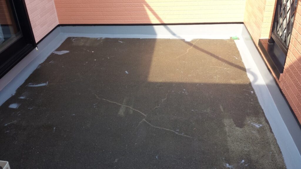 METADATA-START | 外壁塗装は神奈川県横浜市の塗装職人 Flat rooftop/balcony with a dark asphalt surface, visible cracks, and a light gray edge flashing beside brick walls on two sides