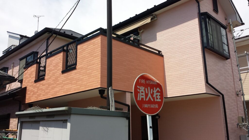 METADATA-START | 外壁塗装は神奈川県横浜市の塗装職人 Peach-colored townhouse with black railings and a round red fire hydrant sign in front of the entrance, displaying Japanese characters and 'FIRE HYDRANT'.