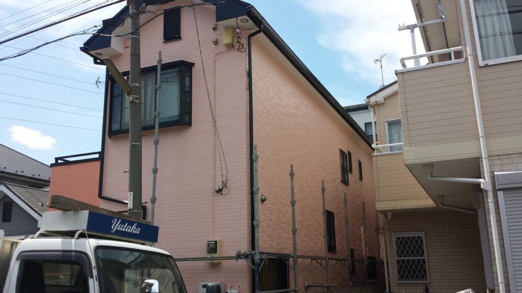 METADATA-START | 外壁塗装は神奈川県横浜市の塗装職人 Peach-colored two-story house under construction with scaffolding along the side and a truck labeled Yutaka in front.