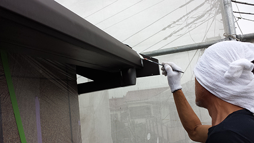 Worker wearing a white head wrap and gloves, painting the edge of a storefront frame with a brush