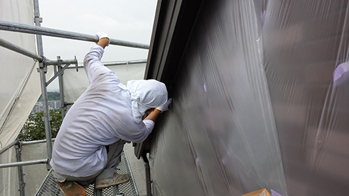 Worker in white hoodie on scaffolding, fastening plastic sheeting to the exterior wall.
