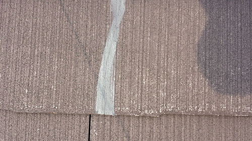 Close-up of brown roof shingles with a vertical gray sealant line along a seam.