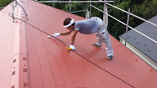Man on a red metal roof with safety rope, wearing gloves and a headband, wiping the surface with a cloth