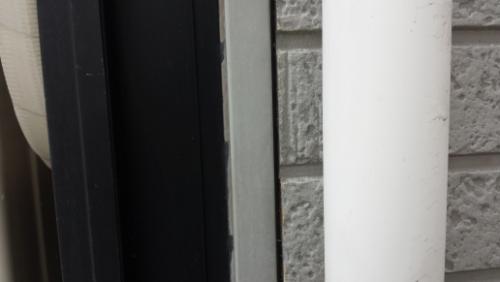20130826-095121 | 外壁塗装は神奈川県横浜市の塗装職人 Close-up of a doorway edge showing a black door frame, metal strip, and a white vertical pipe beside a textured brick wall.
