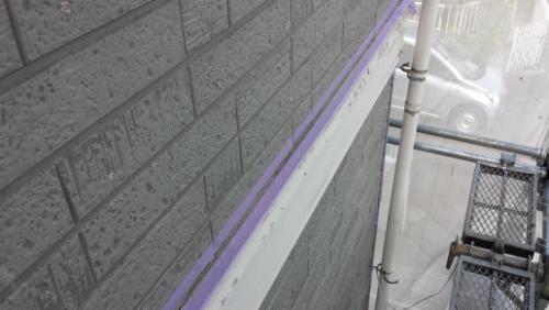 20130827-091530 | 外壁塗装は神奈川県横浜市の塗装職人 Gray brick exterior with purple painter’s tape along a ledge; scaffolding visible on the right side.