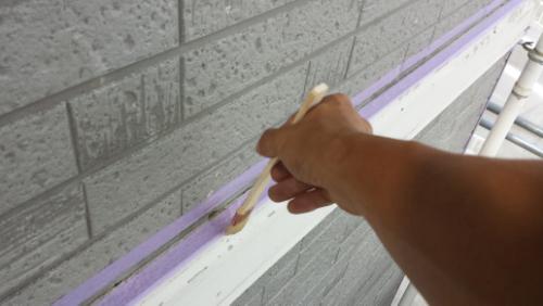 20130827-091545 | 外壁塗装は神奈川県横浜市の塗装職人 Close-up of a hand painting along purple painter’s tape on a gray exterior brick wall.