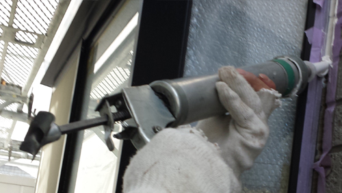 20130828-110643 | 外壁塗装は神奈川県横浜市の塗装職人 Gloved hand holding a caulking gun applying sealant along a window frame.