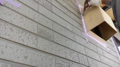 20130828-112151 | 外壁塗装は神奈川県横浜市の塗装職人 Worker wearing gloves applies pink/purple painter's tape around a window opening on a brick exterior wall during a renovation.