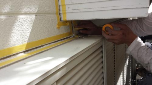 20130831-093215 | 外壁塗装は神奈川県横浜市の塗装職人 Person applying yellow painter's tape along a window frame on an exterior wall, preparing to paint.