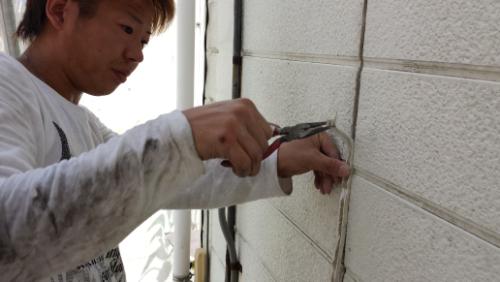 20130831-095159 | 外壁塗装は神奈川県横浜市の塗装職人 Person wearing a light sweatshirt chisels a concrete exterior wall with a metal tool held against the surface