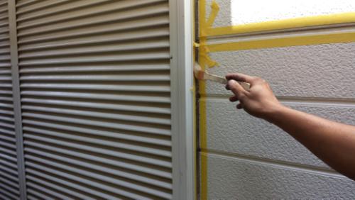 20130831-112627 | 外壁塗装は神奈川県横浜市の塗装職人 Person applies yellow painter's tape along the seam between a vent and a painted exterior wall to prep for painting
