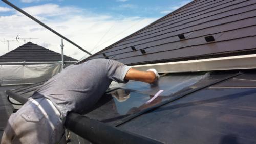 20130902-113232 | 外壁塗装は神奈川県横浜市の塗装職人 Worker on a sloped roof wiping a glass skylight with a cloth.