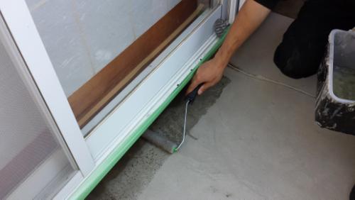 20130912-085308 | 外壁塗装は神奈川県横浜市の塗装職人 Person kneeling by a sliding glass door, applying sealant along the threshold with green painter's tape.