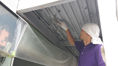 koushin_09kerennow | 外壁塗装は神奈川県横浜市の塗装職人 Maintenance worker in a purple shirt and white headscarf cleans the underside of a corrugated metal ceiling using her hand.