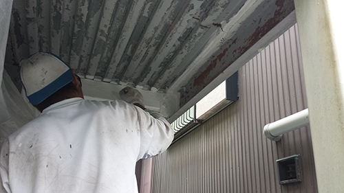 koushin_10sabidome | 外壁塗装は神奈川県横浜市の塗装職人 Maintenance worker in a white shirt and blue cap painting the underside of a metal ceiling outdoors.