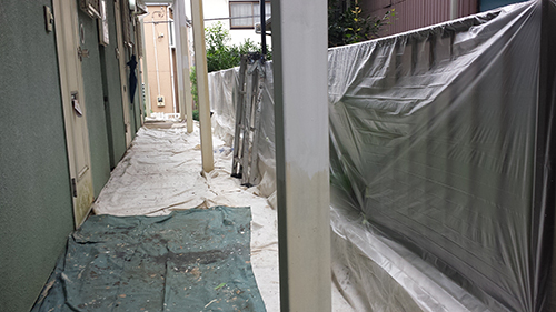 koushin_10youjyou | 外壁塗装は神奈川県横浜市の塗装職人 Narrow alley between buildings with green walls, debris on tarps, and plastic sheeting covering a barrier on the right.