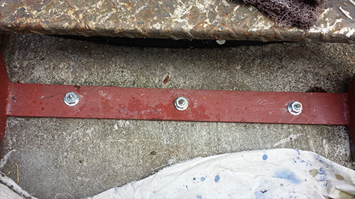 koushin_29bis | 外壁塗装は神奈川県横浜市の塗装職人 Close-up of a red metal strip bolted to a rough concrete surface, with a white tarp at the bottom.