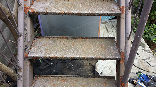 koushin_29hagare2 | 外壁塗装は神奈川県横浜市の塗装職人 Rusty metal outdoor staircase with four steps, rust around the edges, and clutter beneath the steps.