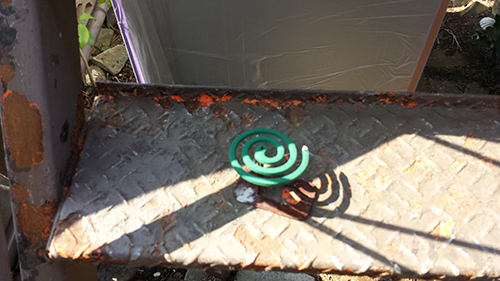 koushin_29senkou | 外壁塗装は神奈川県横浜市の塗装職人 Green spiral coil resting on a rusty diamond-plate metal surface outdoors, with shadows cast nearby.