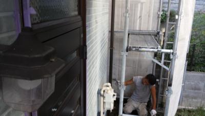 Worker on scaffolding beside the house, kneeling and wearing gloves while performing maintenance near a purple door.