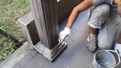 Worker kneeling by a doorway, smoothing concrete at the base of a metal post with a trowel.