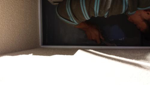 20130930-091931 | 外壁塗装は神奈川県横浜市の塗装職人 Partial view of a person in a blue-striped sweater seen through a window, with sunlight on a beige wall.
