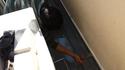 20130930-092315 | 外壁塗装は神奈川県横浜市の塗装職人 Person wearing dark clothing reaching into a metal appliance in a narrow utility space, using a tool (screwdriver) for maintenance.