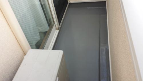 20131003-155003 | 外壁塗装は神奈川県横浜市の塗装職人 Narrow balcony with gray floor, beige walls, a glass sliding door, and a white outdoor air conditioner unit on the left side.