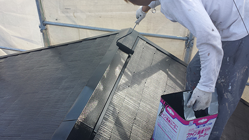 Worker in gloves applying black roof coating with a brush on a sloped metal roof.