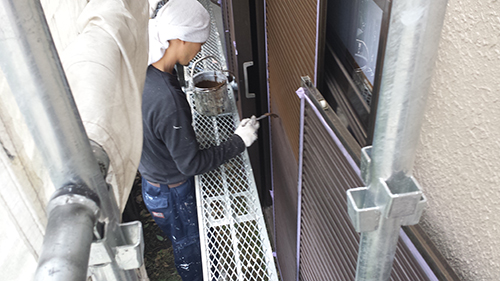 Two construction workers on a metal scaffold painting the frame of a doorway outside a building