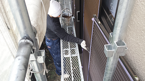 Worker in a white cap and gloves on metal scaffolding, painting the door frame of a building.