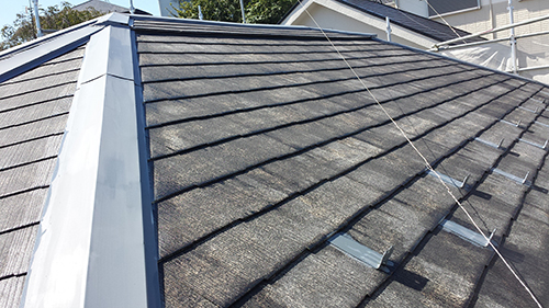 Pitched roof with dark asphalt shingles, a metal ridge cap, and two small roof vents; a few wires run across the surface.