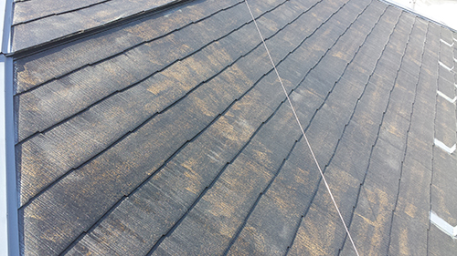 Close-up of a slanted dark shingled roof with diagonal seams and weathered texture.
