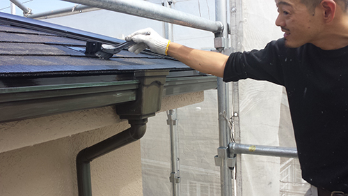 Worker in gloves on scaffolding repairing or cleaning a gutter along a residential roof.
