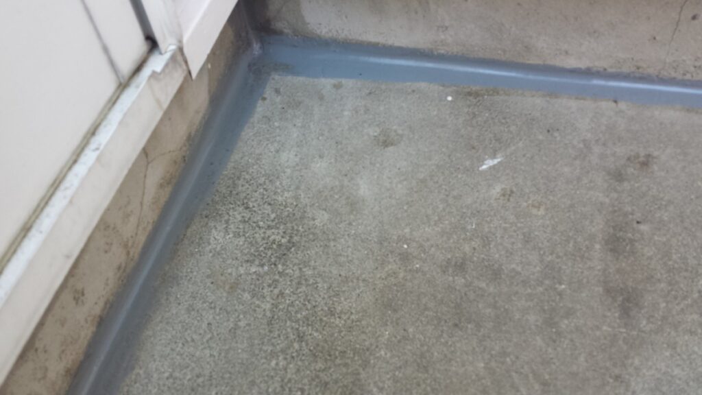 METADATA-START | 外壁塗装は神奈川県横浜市の塗装職人 Close-up of a concrete floor at a corner with a blue-gray painted edge seam where two walls meet.