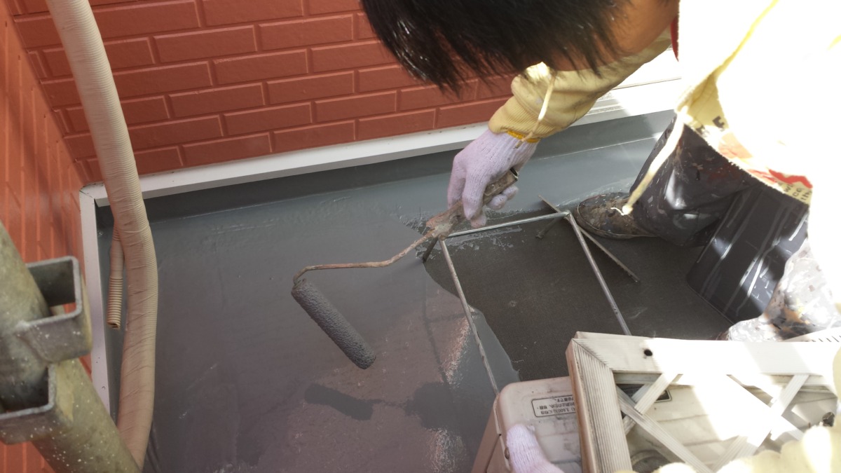 METADATA-START | 外壁塗装は神奈川県横浜市の塗装職人 Person in gloves rolling dark gray paint onto a flat rooftop near a brick wall with a paint roller Assembly line of equipment nearby.