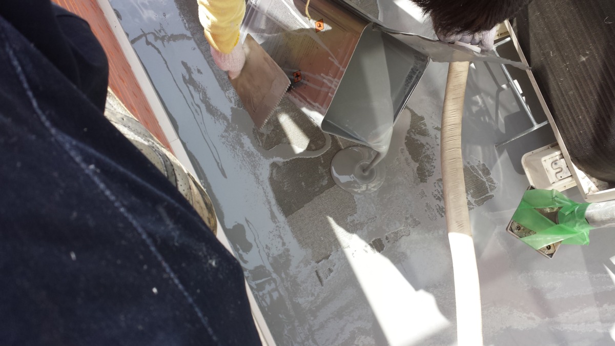 METADATA-START | 外壁塗装は神奈川県横浜市の塗装職人 Worker in yellow gloves smoothing wet cement on a gray metal surface; a metal bucket and hoses nearby on a construction site