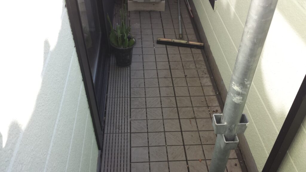 METADATA-START | 外壁塗装は神奈川県横浜市の塗装職人 Narrow tiled balcony or corridor with a potted plant, a broom, and a metal scaffold pole against pale walls.