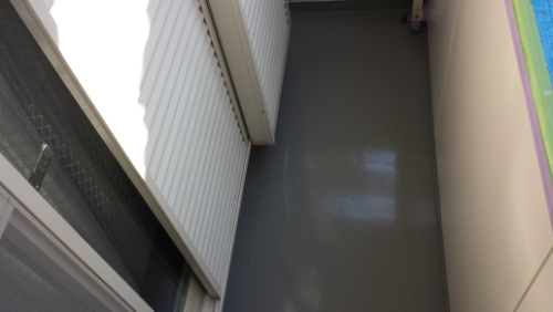 Narrow outdoor balcony or corridor with a glossy gray floor, white radiator on the left, and a bright light source casting shadows.