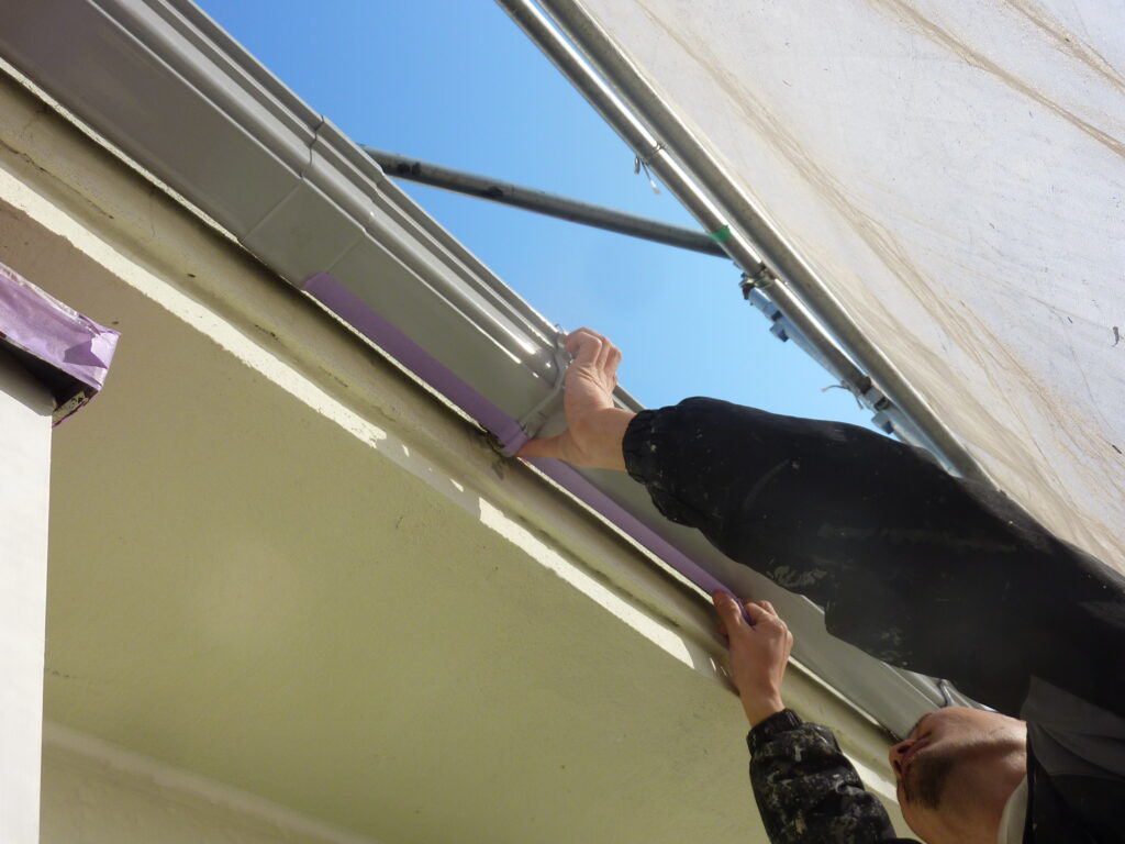 Worker attaching a metal gutter to the edge of a building under a clear blue sky.