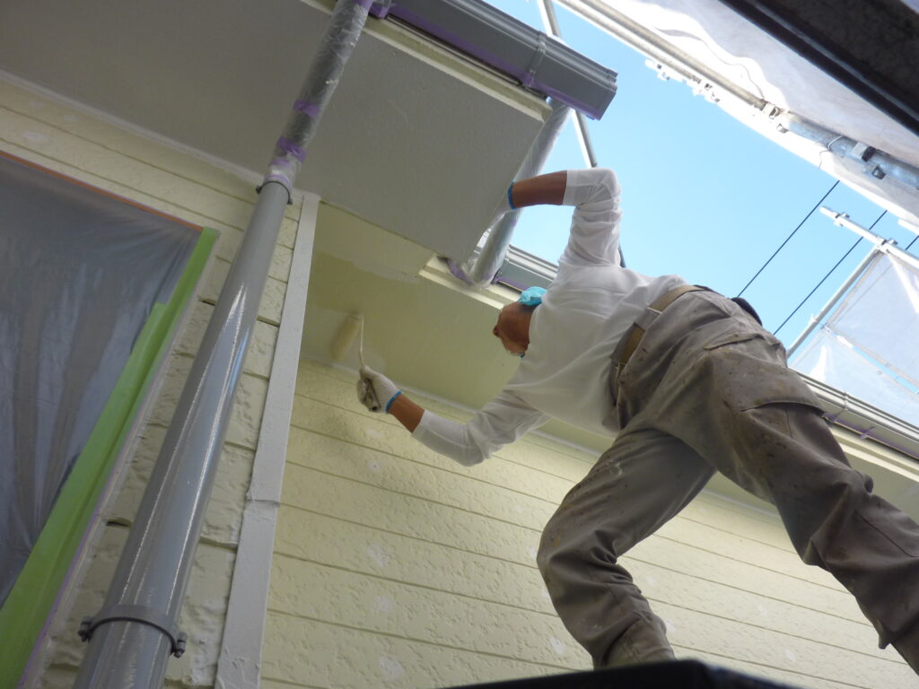 Worker in protective gear painting the exterior wall with a roller on a scaffold