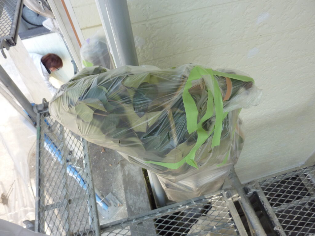 Plastic-wrapped item secured with bright green tape on a metal scaffold, with a person visible in the background during a construction task.