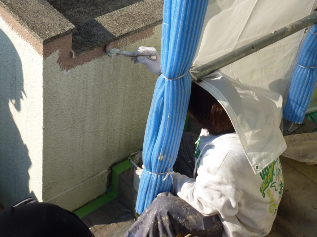 Worker in protective suit and hood applying plaster to a wall with a brush, surrounded by blue tarps and scaffolding.