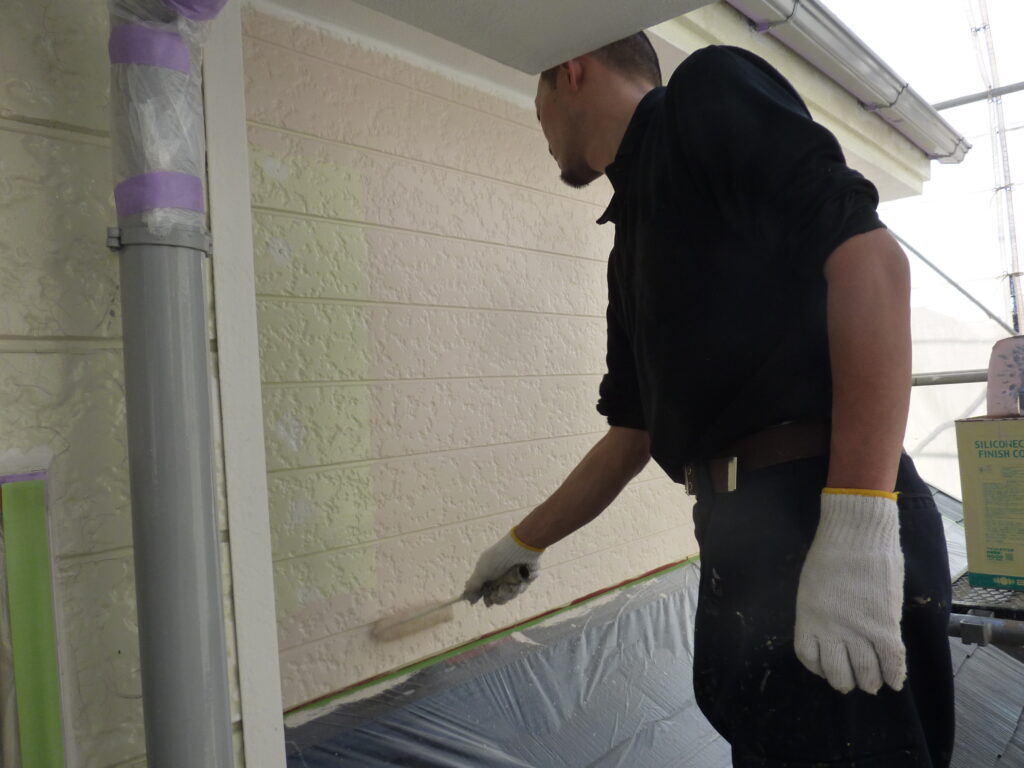 Construction worker painting the exterior wall with a roller, wearing gloves on a scaffold environment