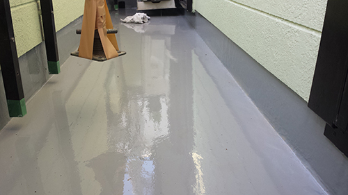 koushin_18uretan2 | 外壁塗装は神奈川県横浜市の塗装職人 Glossy gray epoxy-coated hallway floor with a wet reflection, a wooden sawhorse on the left, and light-green walls.