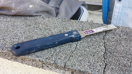 Blue-handled utility knife with extended blade resting on a rough concrete surface