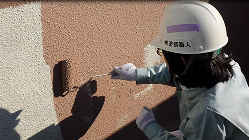 Construction worker wearing a helmet and gloves paints a textured wall with a roller.