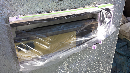 Wall-mounted mailbox still wrapped in protective plastic with painter's tape during installation or renovation, brand name 'National' visible on the unit